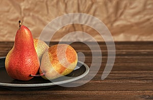 Three ripe pears in a ceramic plate on a wooden background. Organic fruits close up. Space for text. Fresh seasonal produce.