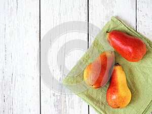 Three ripe red pears against a white wooden background. Top view. Green napkin. Free space for text