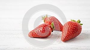 Three ripe strawberries on white wooden table. Isolated strawberry on white background. Summer berry pleasure