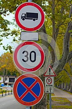 Three road signs on post against old trees. No Goods Vehicles Warning Sign, Speed limit sign and No Stopping sign