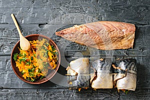 Three rolls of mackerel with vegetables, a bowl of vegetables and sliced fish carcass on a wooden table. The view from