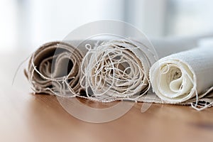 Three rolls of natural linen fabric in different colors with protruding threads on a wooden table