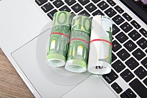 Three rolls of one hundred euro banknotes on a computer keyboard