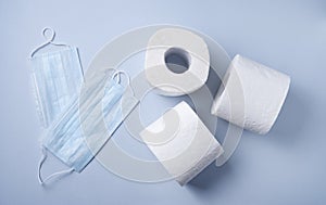 Three rolls of white toilet paper and face masks on a blue background. Pandemic, covid-19, essential goods, scarcity