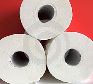 Three rolls of white toilet paper on a red background, hygiene