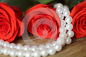 Three roses flowers red with pearl beads on wooden background closeup.