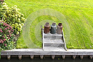 Three rusty metal milk canisters standing on the edge of the canal in the lawn.