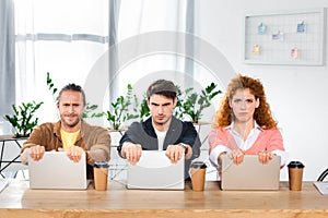 Three sad friends sitting at table and holding laptops