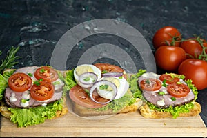 Three Sandwich with ham and tomatoes on wooden board