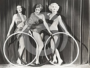 Three scantily clad women holding large rings