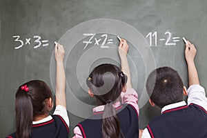 Three school children doing math equations on the blackboard