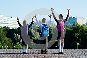 Three schoolchildren amicably walking in the park, and raise their hands upwards