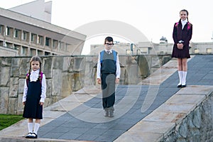 Three schoolchildren of different ages, stand with backpacks behind their back, in school uniforms