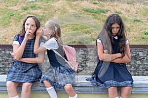 Three schoolgirls are sitting in the schoolyard. One child is offended. The problem of adaptation and communication at