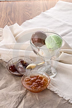 Three scoops of chocolate, pistachio and vanilla ice cream and berry jam in glass bowl on white napkin