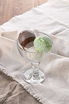 Three scoops of chocolate, pistachio and vanilla ice cream in glass bowl on white napkin