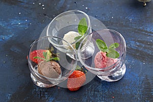 Three scoops of chocolate, strawberry and vanilla ice cream in glass bowl on blue background