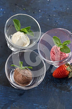 Three scoops of chocolate, strawberry and vanilla ice cream in glass bowl on blue background