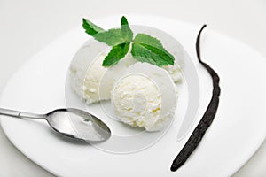 Three scoops of ice cream with mint and a vanilla bean on a white plate, white background