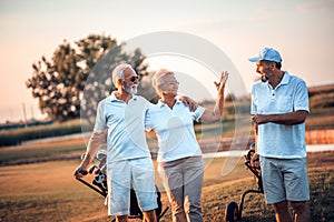 Three senior golfers walking. Focus is on foreground.  The woman greets her friend