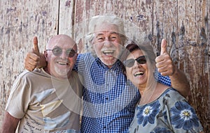 Three senior people together standing in front to an old wooden door laughing happy - active retired elderly and fun concept