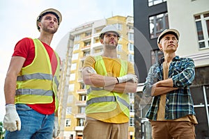 Three serious handsome workers in hardhats staring into the distance