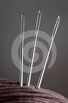 Three sewing needles are inserted into a spool of thread. close-up.
