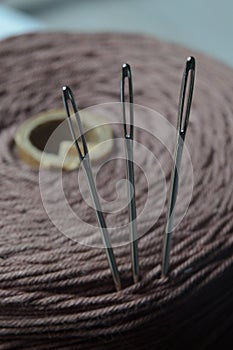 Three sewing needles are inserted into a spool of thread. close-up.