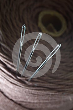 Three sewing needles are inserted into a spool of thread. close-up.