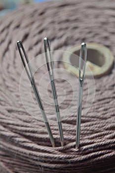 Three sewing needles are inserted into a spool of thread. close-up.