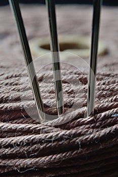 Three sewing needles are inserted into a spool of thread. close-up