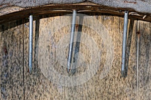 three sharp gray iron nails sticking out of a brown wooden plank