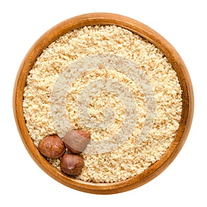 Three shelled hazelnuts on hazelnut meal in wooden bowl