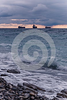 The three ships sails on the sea horizon. Stone coast and sea waves in the foreground