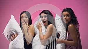 Three shocked women in pajamas holding pillows, watching horror movie at night