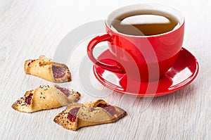 Three shortbread cookies with jam, cup with tea on saucer on table