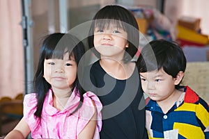 Three sibling held a photo together. Asian cute girl smiles sweetly, the boy does not look at the camera.