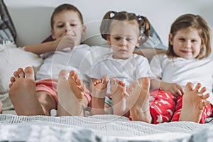 Three siblings lie on bed with bare feet. Focus on legs of the children. Two girls and a boy, friends or family