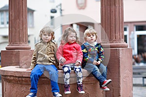 Three siblings sitting together on fountain in city