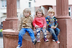 Three siblings sitting together on fountain in city