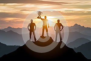Three silhouettes on peak, one with trophy, celebrating achievement with stunning sunrise over mountains