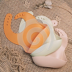 Three silicone baby bibs of different colors on beige blanket. Flat lay. Square frame, instagram use