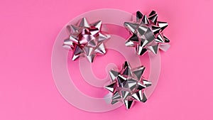 Three silver gift bows spinning on a pink background