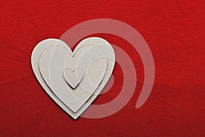 Three silver wooden hearts on red cloth background. Three hearts of different sizes lie on each other. Symbol of three