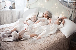 Three sisters in the bedroom in the morning. Girls in pajamas on the bed.