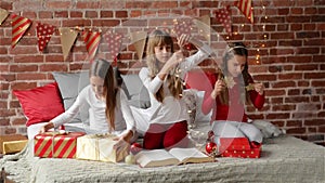 Three sisters dressed in xmas pajamas sitting on a decorated bed for the Christmas, triplet girls opening presents