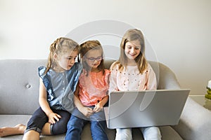 Three sisters girls sit on the sofa at home with laptop