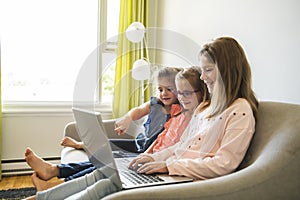 Three sisters girls sit on the sofa at home with laptop