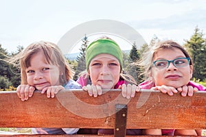 Three sisters on a mountain trip hiding behind a fence - forest and mountains in the background behind them