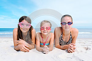 Three sisters on a seaside beach lying on their bellies in swimming goggles and swimwear